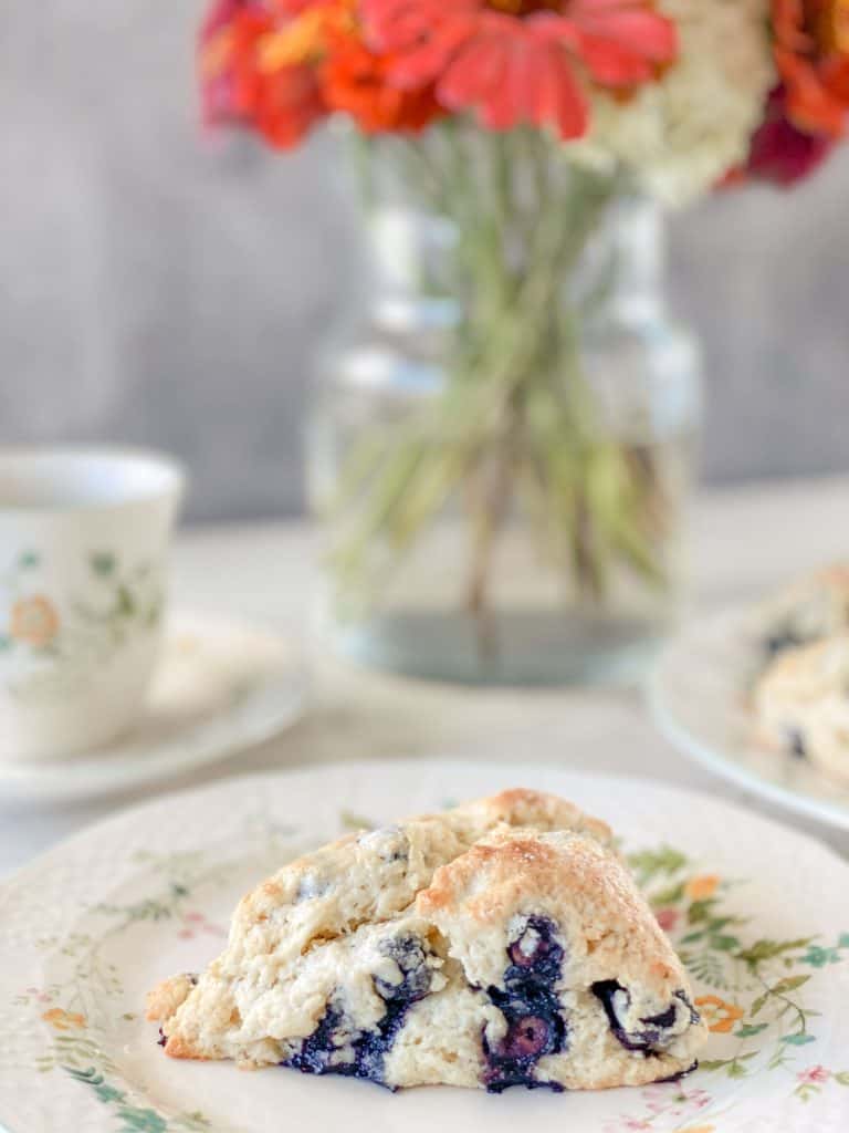 sourdough blueberry scone on plate with flowers in vase in background