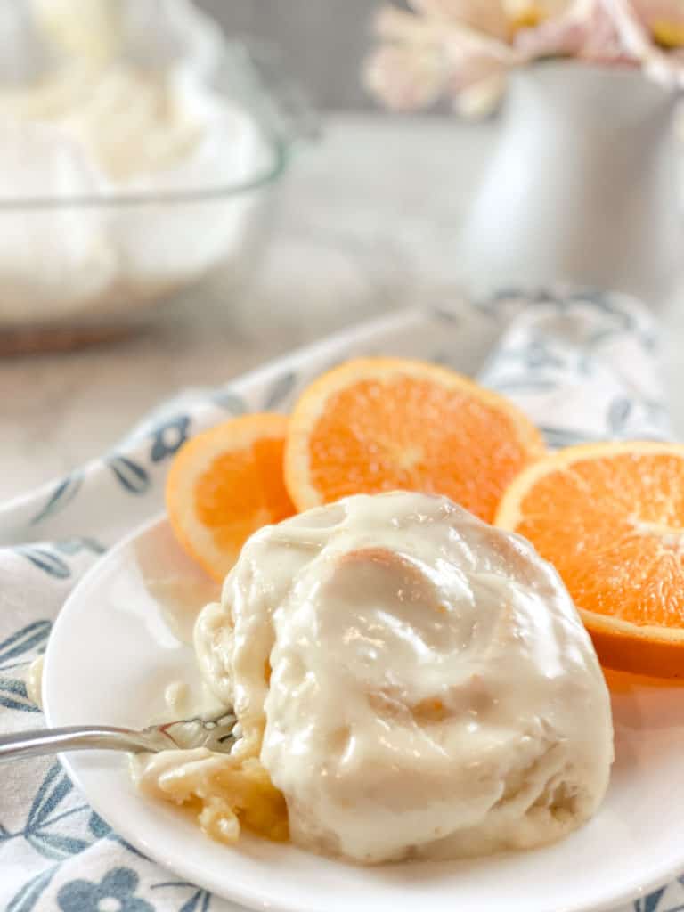 sourdough orange roll on white plate with sliced oranges and flowers in a vase in background