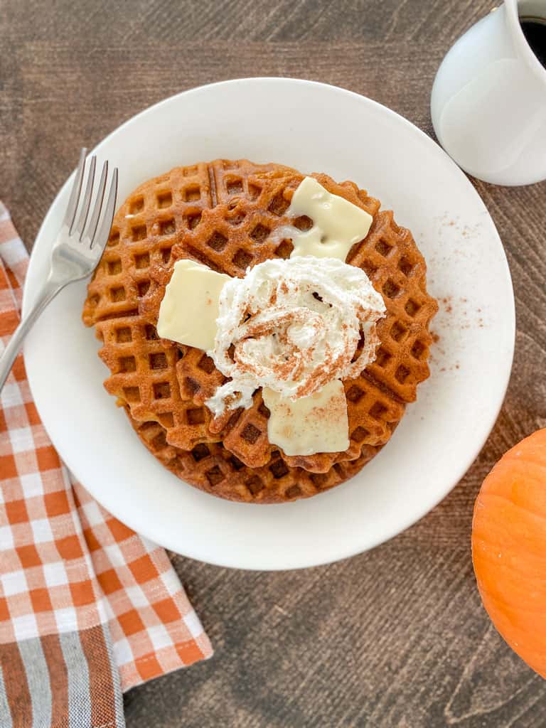 pumpkin sourdough waffle on plate topped with maple syrup butter whipped cream