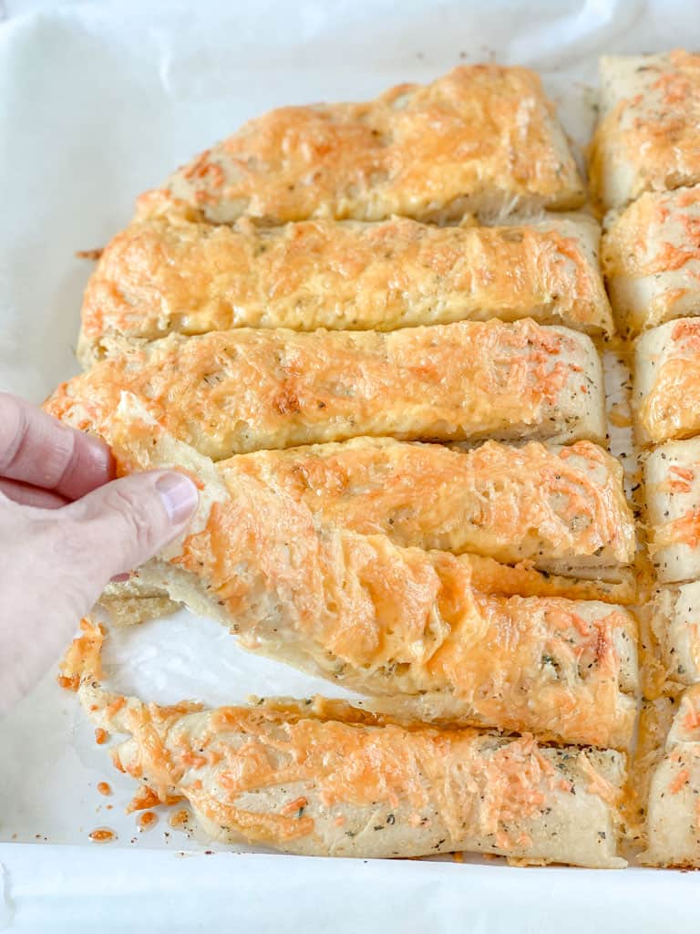 breadsticks on countertop with hand picking up one breadstick